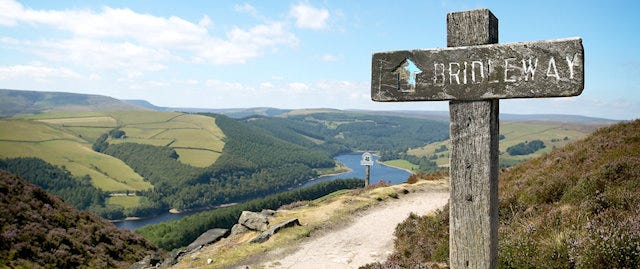 Old wooden signpost points to a bridleway that overlooks a valley
