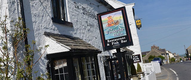 A sign hangs from the outside of a country pub