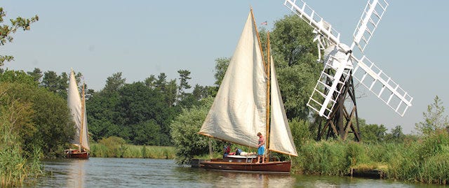 A family sailing past an old windmill on the Norfolk Broads