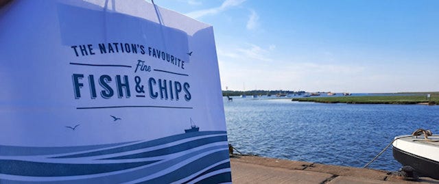 bag of fish and chips with the sea in the background