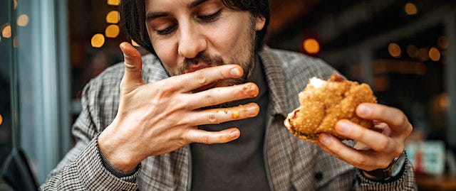 Man enjoying a messy burger. The sauce is all over his fingers