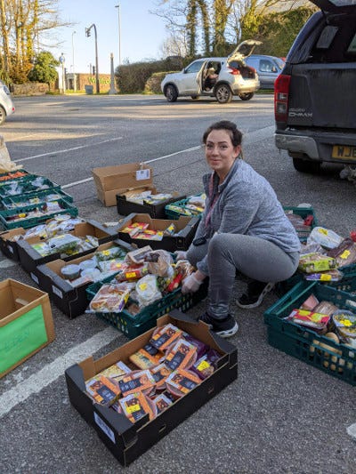 An adult crouching amongst several boxes of donated food