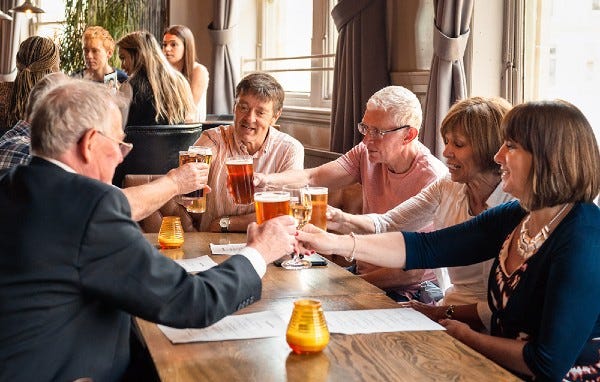 Group of adults all sitting around table with glasses raised to cheers 