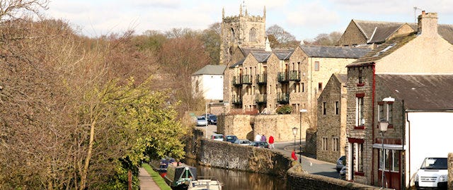 View of a Church behind buildings and the river at Skipton