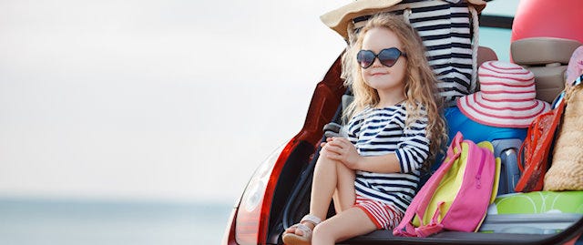 Child sitting on the edge of a packed boot of car