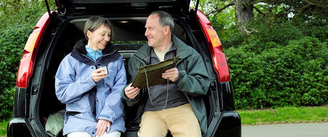 Middle-aged couple sitting on the back of their car, looking at a map