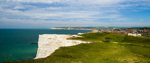 walkers on grassland near a cliff edge that overlooks the sea