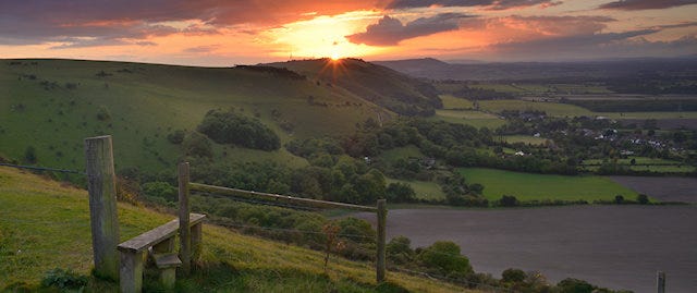 Sun setting behind a distant hilltop, with a lake below