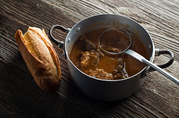 Metal pan with meat stew and a half baguette of bread
