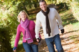 A smiling middle-aged couple, holding hands, laughing, walking through the woods.