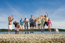 A smiling family of all ages jumping in the air by the seaside.