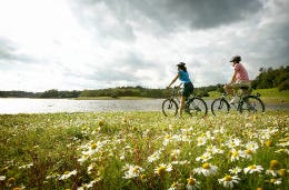 Couple cycling through green fields in the sun.