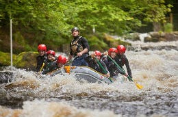 Friends smiling as they go white water rafting on rapids on Tryweryn River in Wales