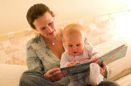 A new mum in a holiday cottage reading a book to her happy baby