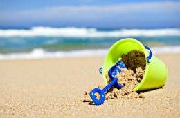 Green bucket and blue spade on a beautiful sandy beach with blue sea in the background