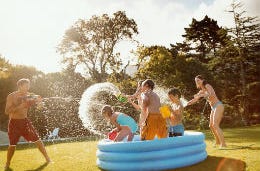 Five Fun Games to Play in a Swimming Pool Large family having fun playing with water pistols in a paddling pool