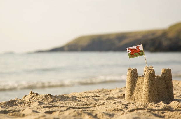A sand castle on the beach with a Welsh flag in it and the sea and sky behind.