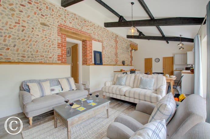 Open plan living room with comfortable seating, exposed brickwork & beams.